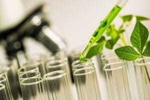 pipette over test tube dropping sample chemical into sample herbal plaint with microscope background , biotechnoloy research concept
